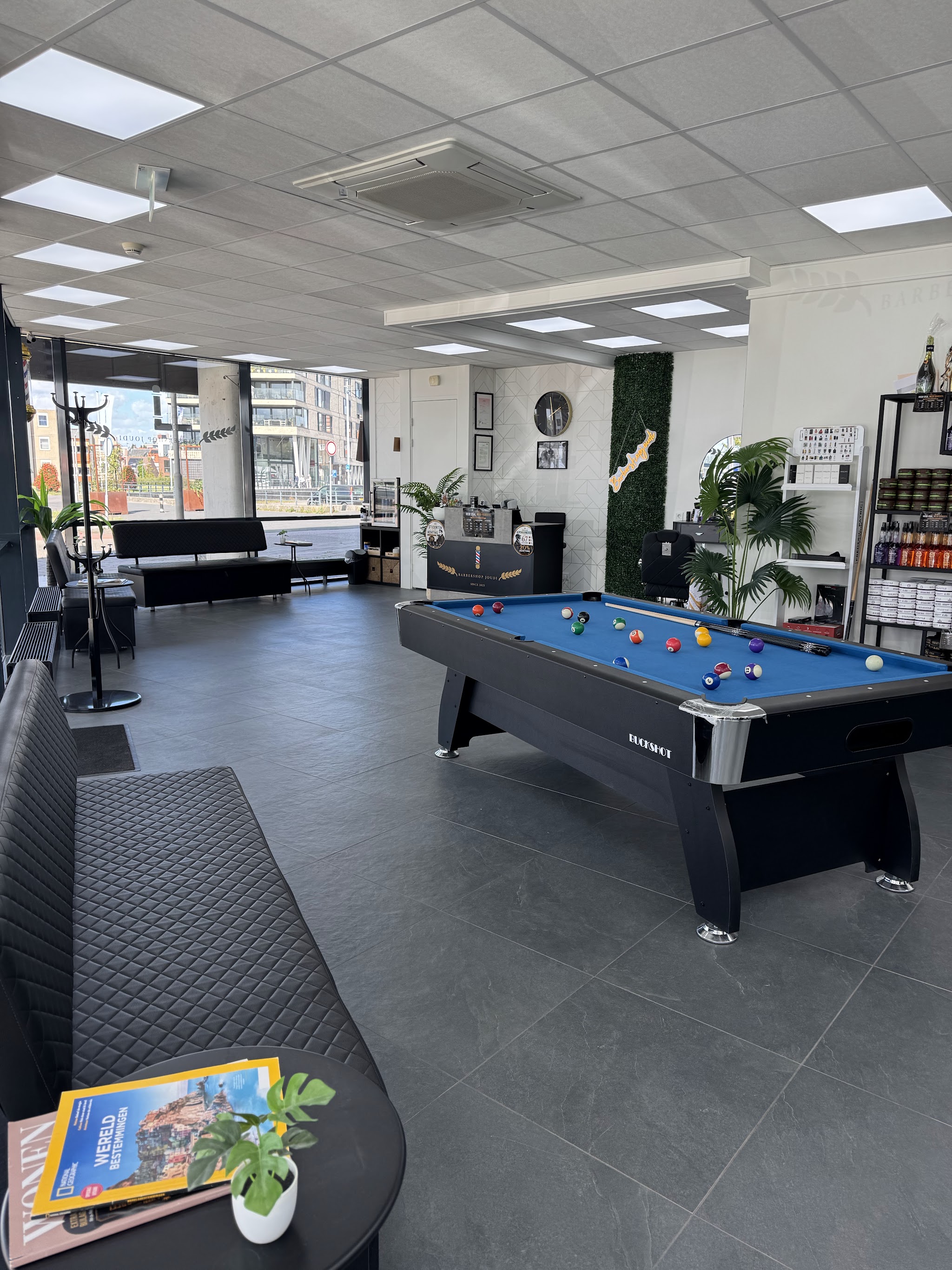 Wachtruimte met pooltafel en planten bij Barbershop Joudi